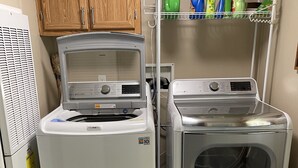Un espace buanderie comprenant deux machines à laver, un meuble en bois et une étagère avec des produits de nettoyage.