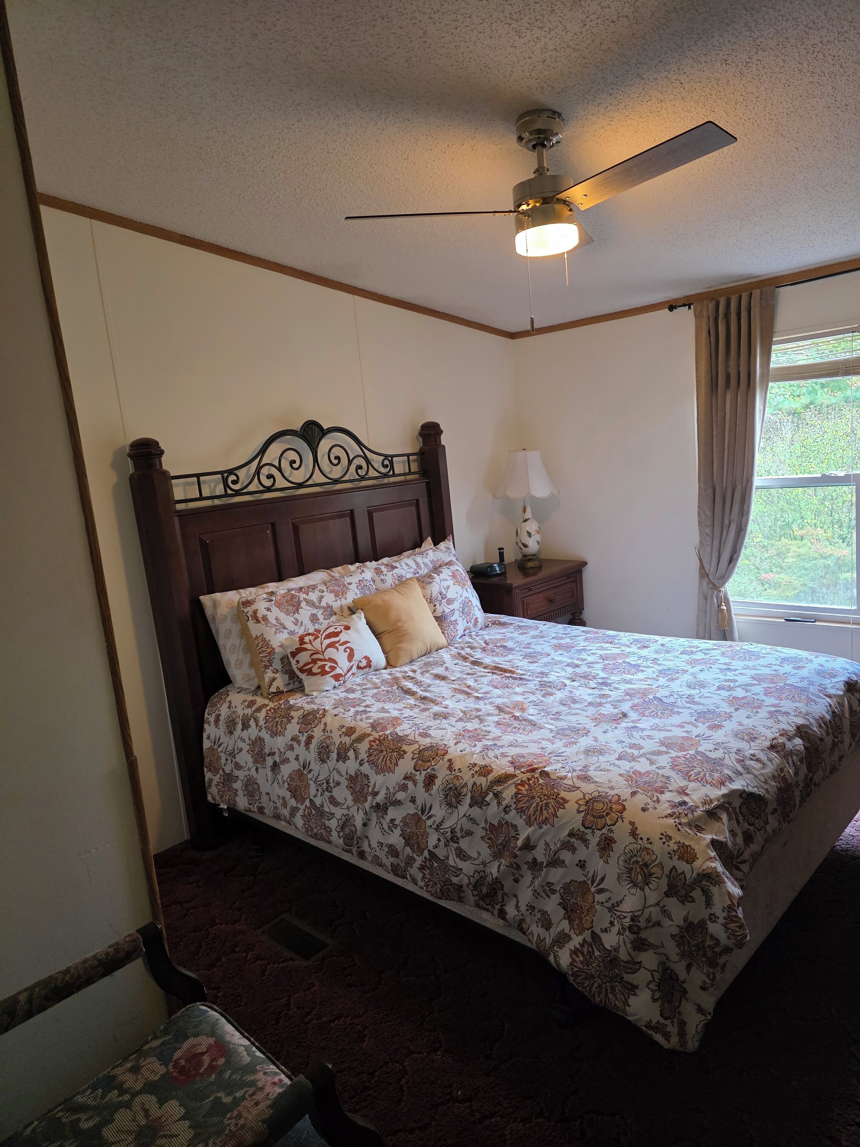 A bedroom with a bed, a nightstand, a lamp, a ceiling fan, and a window with curtains.