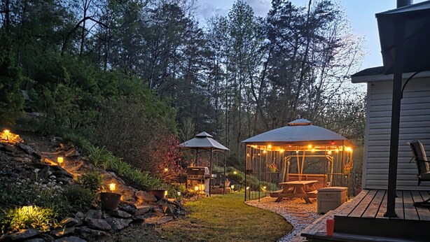 Un jardin avec un belvédère, un espace barbecue et une terrasse en bois.