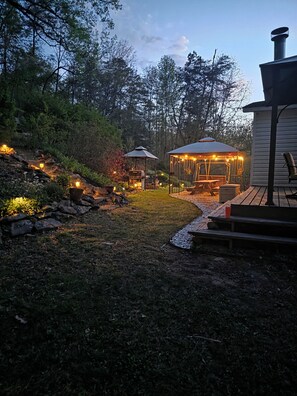 Un jardin avec un belvédère, un espace barbecue et une terrasse en bois.