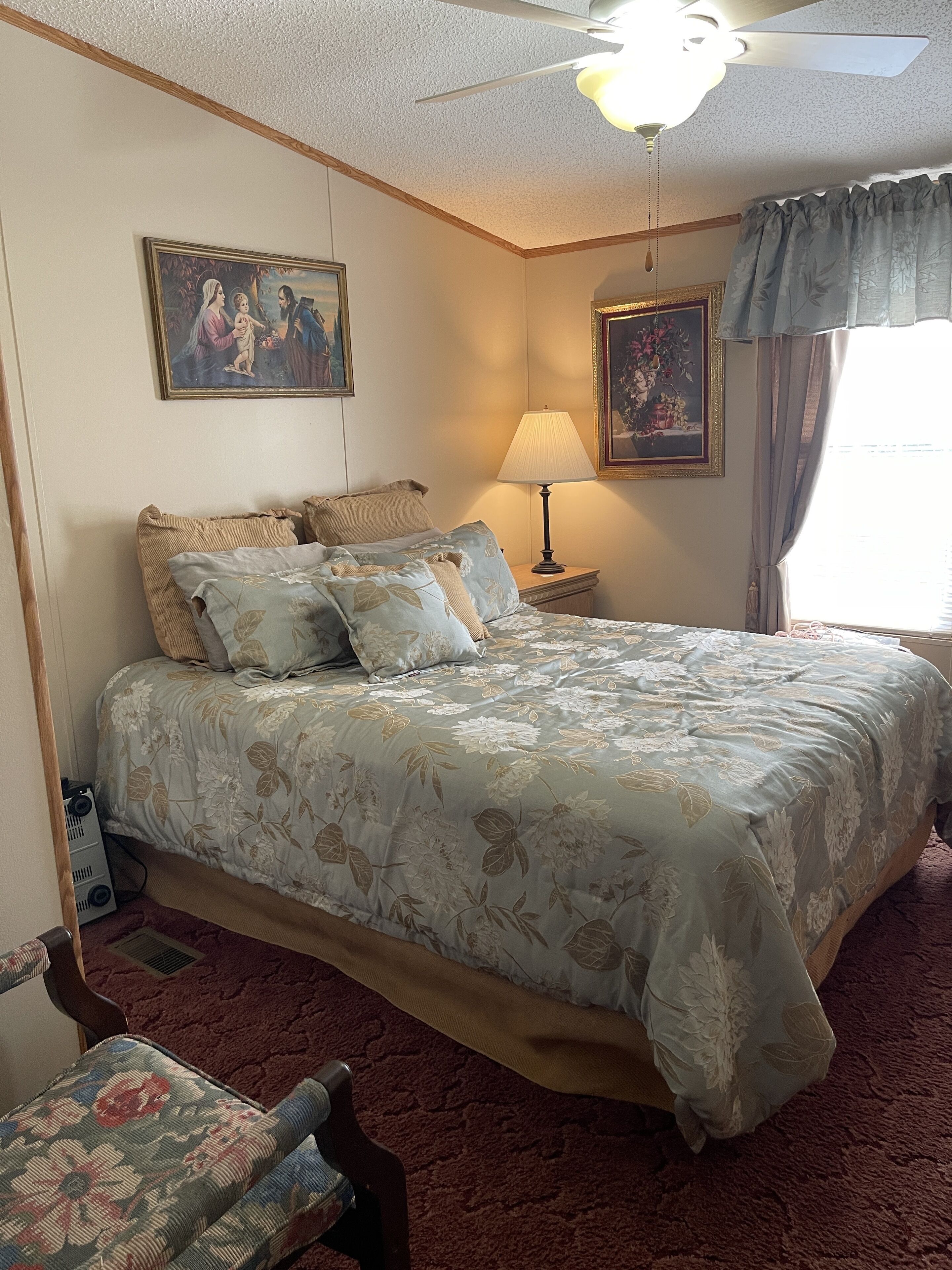 A bedroom with a bed, a nightstand, a lamp, a chair, and two paintings on the wall.
