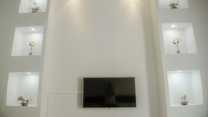 A modern living room with a flat-screen TV mounted on the wall, surrounded by recessed lighting and small square shelves with decorative items. - La Puerta Azul (Santa Marta)