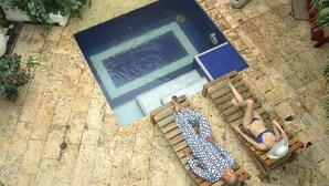 A pool area with two wooden loungers, one occupied by a person in a patterned outfit and another by a person in a bikini. - La Puerta Azul (Santa Marta)