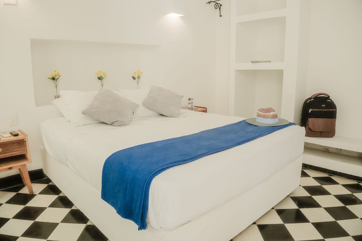 A neatly made bed with a blue blanket, white pillows, and a small vase with yellow flowers on the nightstand.