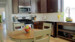 A modern kitchen with dark brown cabinets, a stainless steel microwave, a gas stove, and a dining area with a wooden table and chairs. - Bright Upper-Level 3BR Chicago • King • Walkable (Chicago)