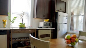 A kitchen with dark cabinets, a microwave, a refrigerator, a wooden table with a bowl of fruit, and a window with blinds. - Bright Upper-Level 3BR Chicago • King • Walkable (Chicago)