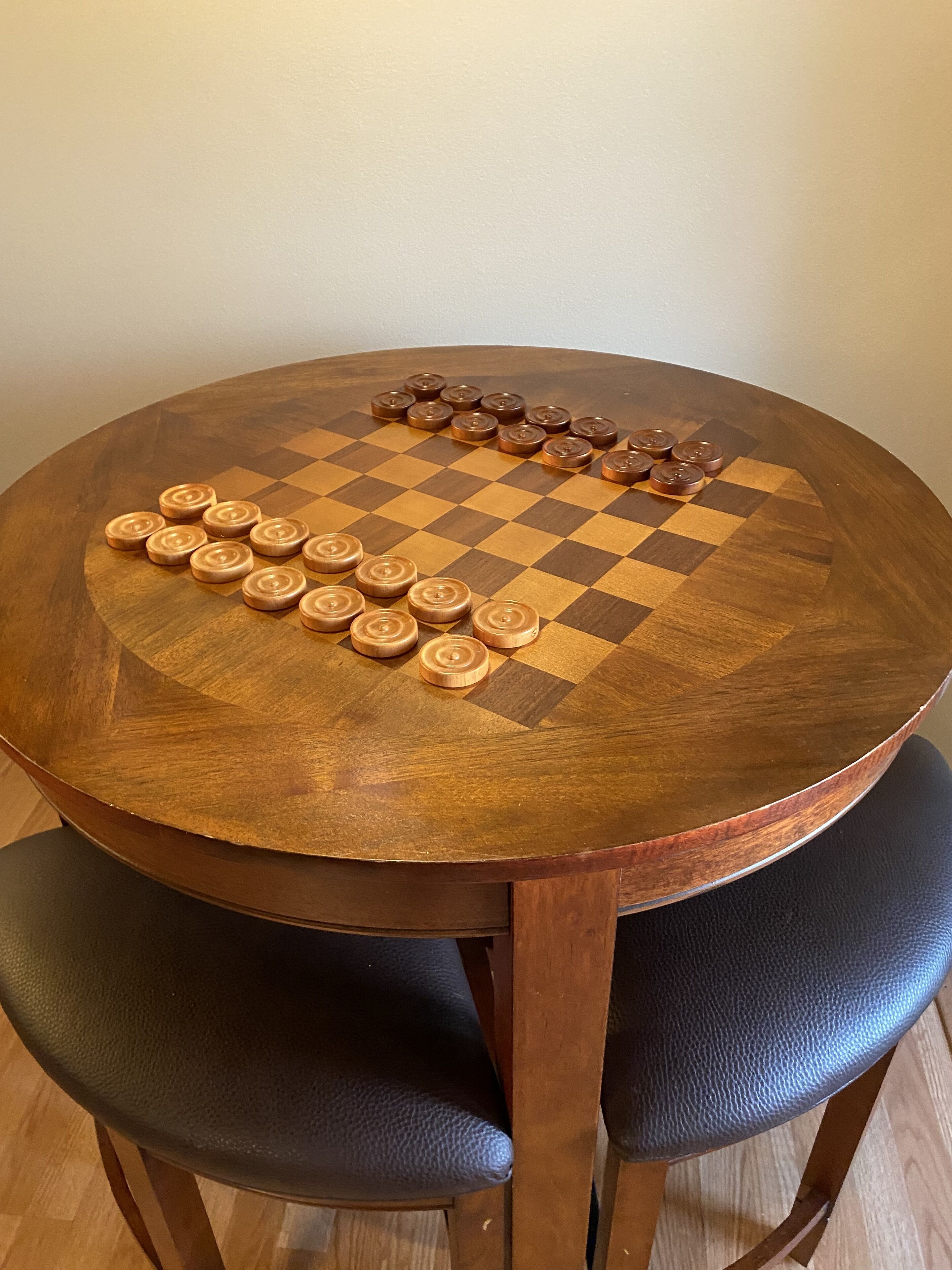 Uma mesa de madeira redonda com um tabuleiro de xadrez quadriculado e peças de xadrez.