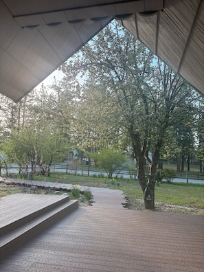 Un espace extérieur abrité, doté d’un chemin en bois menant à un coin salon, entouré d’arbres et offrant une vue sur une étendue d’eau.