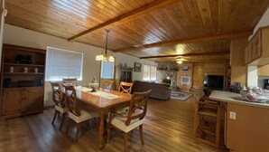 Amplia sala de estar con techo de madera, chimenea de piedra y comedor con mesa y sillas de madera.