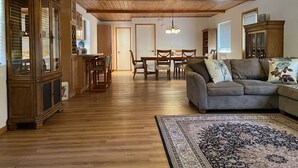 Un salón amplio con techo de madera, un comedor con mesa y sillas de madera, y un sofá grande con cojines decorativos.