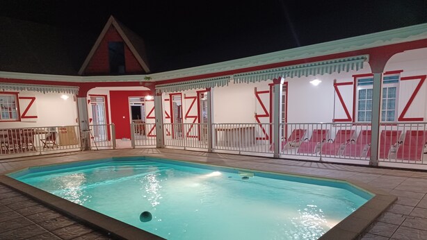 Una piscina interior amb paviment de rajoles, envoltada per una zona tancada amb parets blanques i vermelles i un edifici amb teulada vermella al fons.