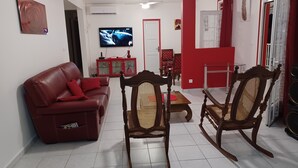Un saló amb un sofà vermell, cadires de fusta, un televisor i un armari vermell.