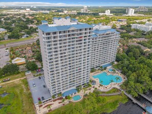 A high-rise hotel with multiple balconies, a swimming pool, and a landscaped area with palm trees. - Lakefront Resort in Heart of Orlando Attractions - Tu Casa Vacations (Orlando)