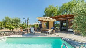 A swimming pool with lounge chairs and umbrellas, surrounded by trees and a pergola.