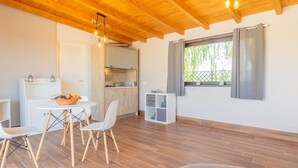 A modern, open-plan living space with a wooden ceiling, a dining area with a table and chairs, a kitchen with a built-in oven, and a window with curtains.