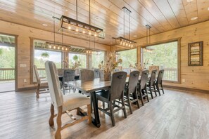 A spacious dining area with a long wooden table, multiple chairs, and pendant lighting.