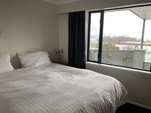 Relax in a serene space with a large bed and floor lamp, offering a view of the surrounding neighborhood.