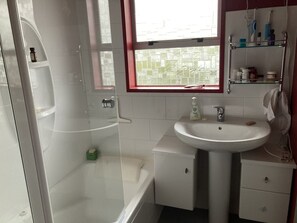 Bathroom features a glass-enclosed shower, sink with soap dispenser, and mirror.