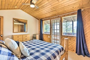 Un dormitorio con techo de madera, una cama con colcha a cuadros, un aparador, un espejo y una ventana con cortinas.