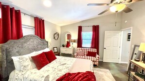 A bedroom with a large bed, a ceiling fan, a dresser, a mirror, and a window with red curtains. - Muleshoe Room in Red Oak Lodge @ Towering Oaks b&b (Valley View)