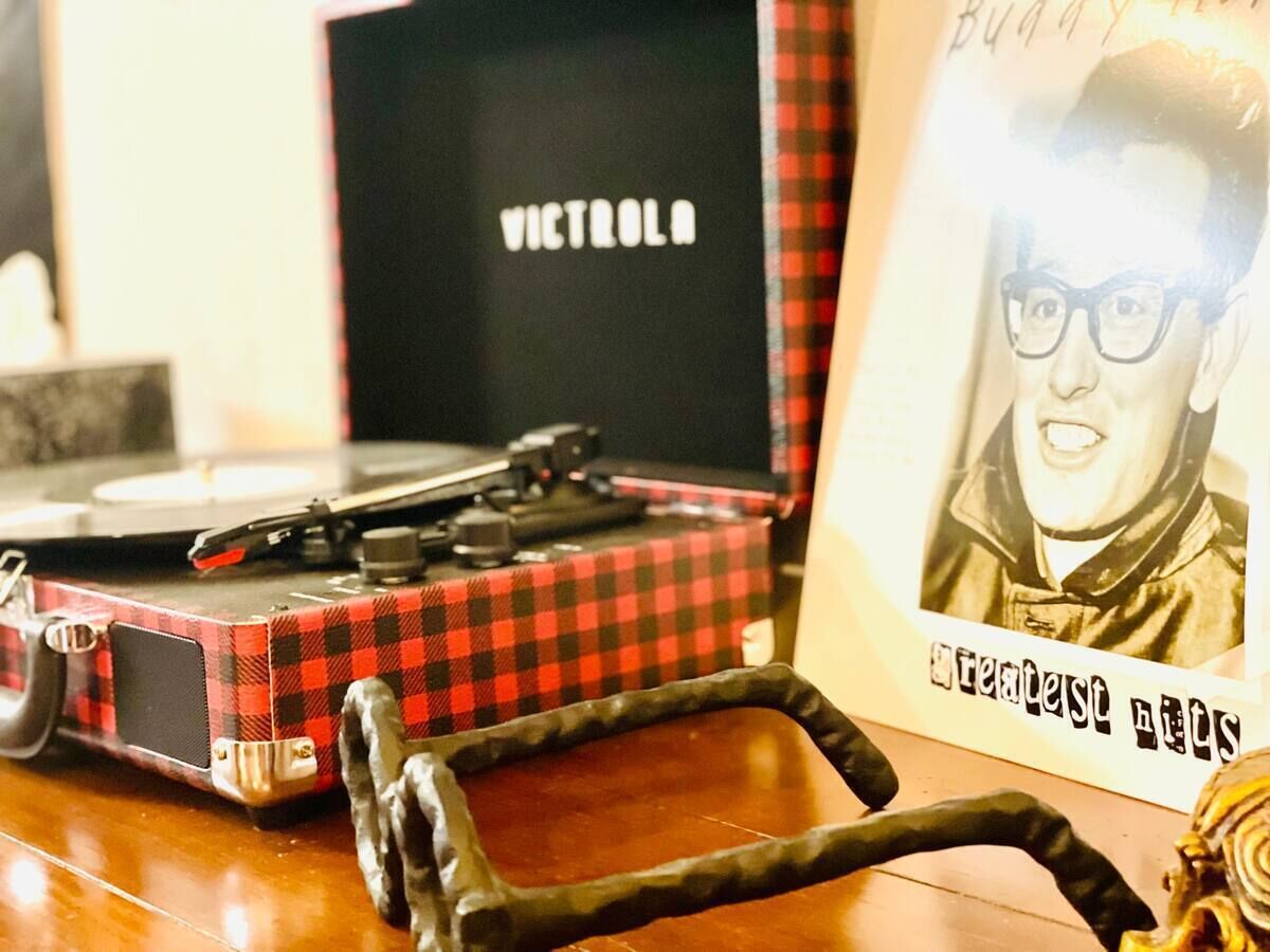 Um toca-discos de vinil com capa xadrez, um par de fones de ouvido e um pôster emoldurado com texto.