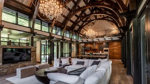 A spacious living room with a large white sectional sofa, a stone fireplace, and a kitchen area visible through an open archway.