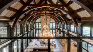 A spacious interior with a high ceiling, wooden beams, large windows, and a central chandelier.