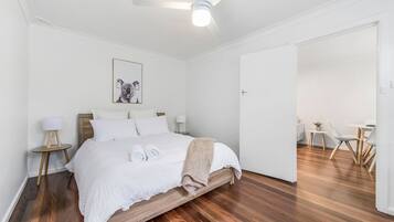 Ein Hotelzimmer mit einem hölzernen Bett, weißer Bettwäsche, einer Koala-Zeichnung, einem kleinen Tisch mit einer Lampe und einem Essbereich mit Stühlen.