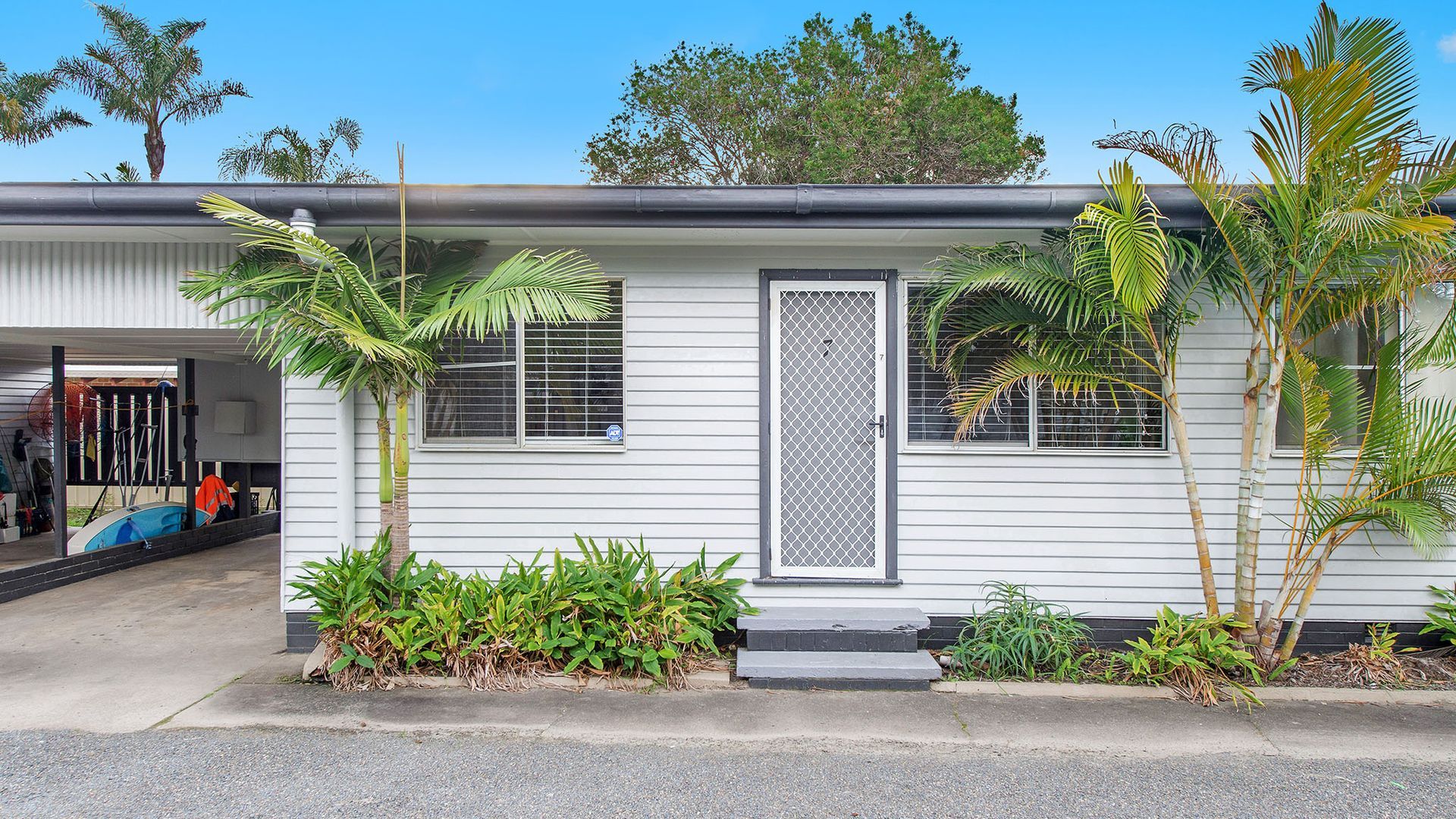 A single-story house with a garage, a covered porch, and a small front yard with palm trees and shrubs.