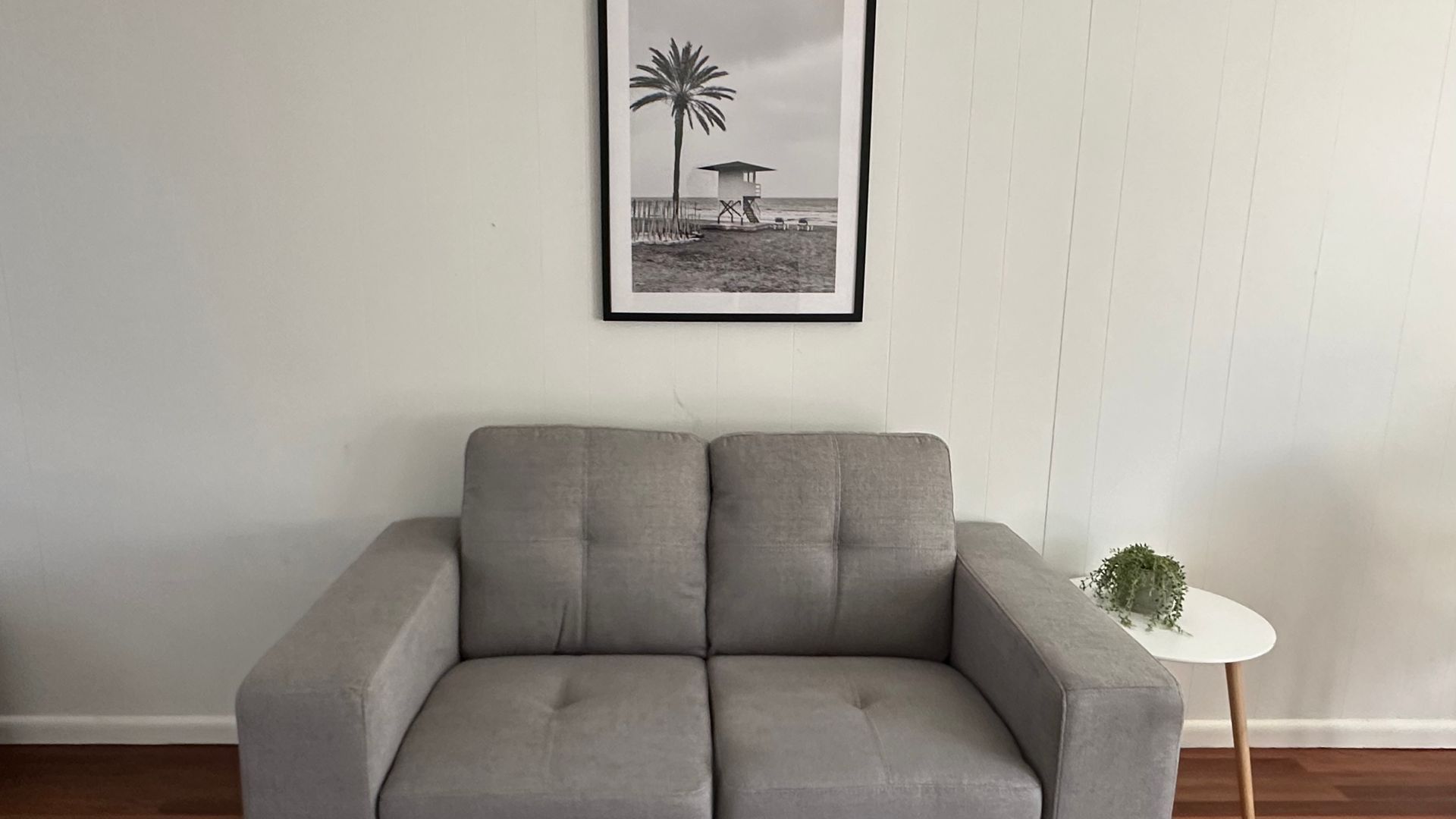 A grey sofa in a room with a framed black and white beach photograph on the wall.