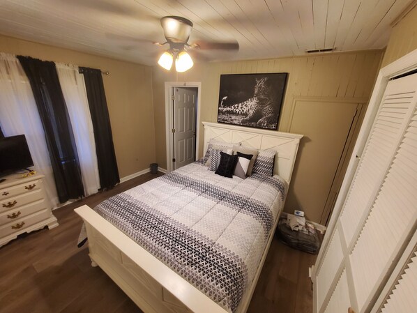 Une chambre à coucher comprenant un lit, une commode, un ventilateur de plafond, une porte et une œuvre d’art à motifs léopard accrochée au mur.