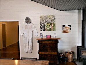 A room with a wooden bench, a small table with a tissue box, a basket, and a wall with a framed picture and a white garment hanging.