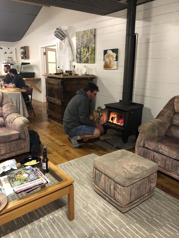 A cozy living room with a fireplace, comfortable seating, and a wooden coffee table with magazines and a bottle.