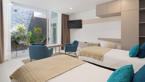 Moderni hotellihuone, jossa on kaksi sänkyä, seinälle asennettu televisio, kasveilla koristeltu parveke ja oleskelualue tuoleineen.