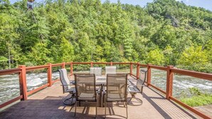 A wooden deck with a table and chairs overlooking a river, surrounded by a red railing.