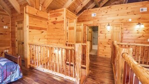 A wooden cabin interior with a bed, a wooden railing, and a staircase.