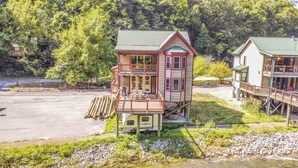 A two-story cabin with a balcony, situated by a river with a dock.