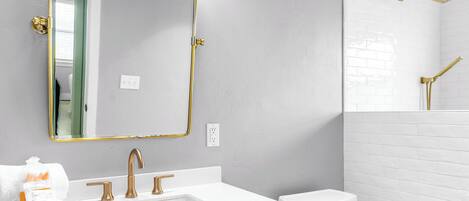 A bathroom with a white vanity, a gold-framed mirror, and a white toilet.