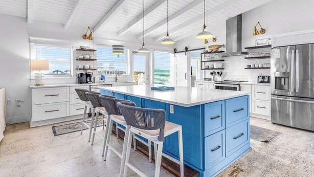 Una cocina moderna con una isla central, taburetes de bar, iluminación colgante y electrodomésticos de acero inoxidable.