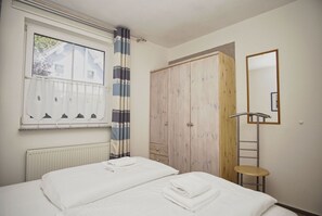 A bedroom with a bed, a window with curtains, a wardrobe, a mirror, and a radiator.