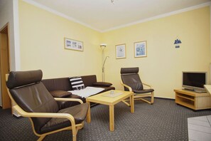 Una habitación con un sofá, dos sillones, una mesita, un televisor y cuadros en la pared.