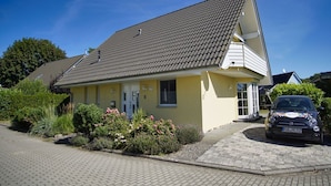 Une maison à deux étages, avec un toit recouvert de tuiles, un porche à l’avant et une voiture garée.
