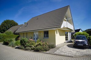 Une maison à deux étages, avec un toit recouvert de tuiles, un porche à l’avant et une voiture garée.