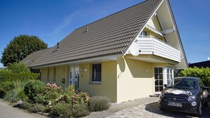 A two-story house with a sloped roof, a satellite dish, and a parked car in the driveway. - Die Ferienwohnung Nr. 02 im Haus Inselblick - Haus Inselblick (Göhren)