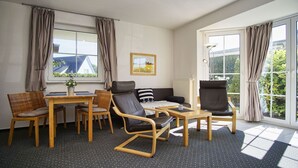 A modern room with a sofa, two armchairs, a dining table, and a window with curtains. - Die Ferienwohnung Nr. 02 im Haus Inselblick - Haus Inselblick (Göhren)