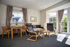 Ein modernes Zimmer mit einer Couch, zwei Sesseln, einem Esstisch und einem Fenster mit Vorhängen.
