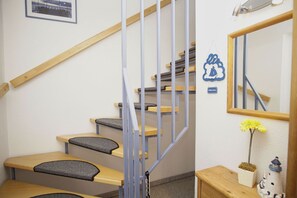 A staircase with wooden steps and metal railings, a small table with a chair, a mirror, and a welcome sign.