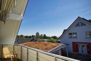 Un balcon donnant sur un immeuble aux couleurs rouge et blanc, avec une chaise et un toit végétalisé.