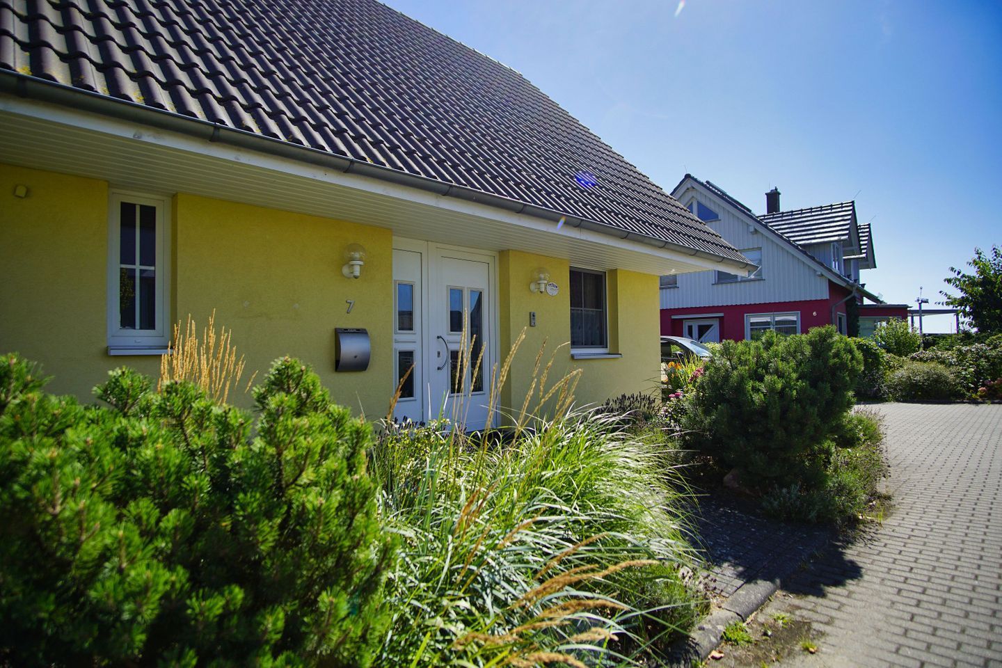 Un bâtiment jaune avec un toit recouvert de tuiles, une boîte aux lettres et le numéro « 7 » sur la porte.