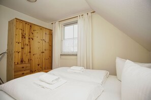 Une chambre avec deux lits, une armoire en bois et une fenêtre avec des rideaux.